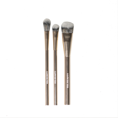 Three makeup brushes with metallic handles and gray bristles, arranged vertically on a plain white background. The handles are printed with the brand name 'REL BEAUTY'