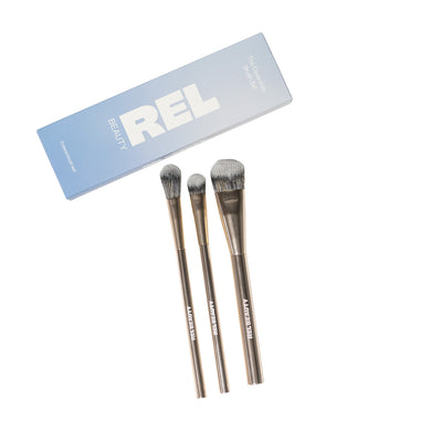 Three makeup brushes with metallic handles and gray bristles, displayed next to their light blue and white REL BEAUTY packaging box on a solid white background.